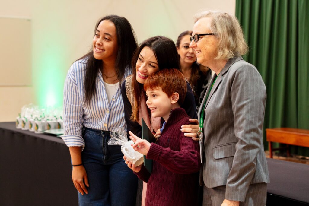 Professores e membros da equipe pedagógica posam sorrindo ao lado de um aluno durante o evento escolar